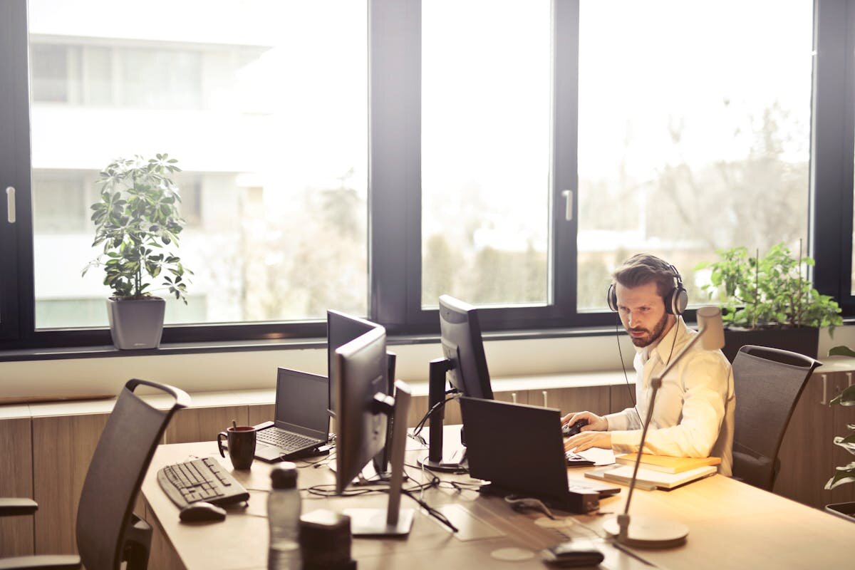 Customer support representative with headphones facing multiple monitors - Photo by Olly