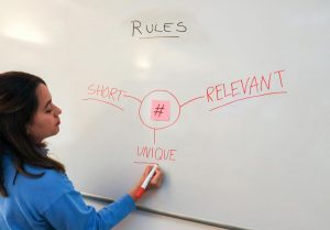 Marketing Specialist Writing Out the Rules Around a Sticky Note with a Hashtag on the Whiteboard