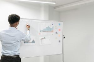 A Man in Long Sleeve Shirt Writing on White Board